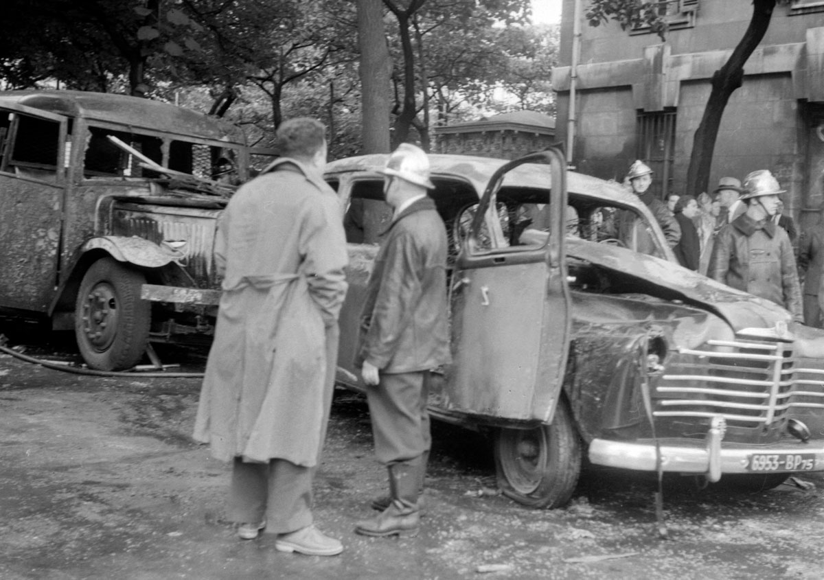 Des pompiers devant les carcasses calcinées d'une voiture et d'un car de police, le 15
         juillet 1953 à Paris.